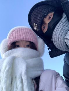 two people wearing hats and scarves standing next to each other in the snow outside