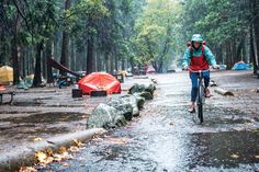 a person riding a bike in the middle of a forest with tents set up behind them