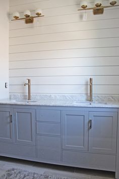 a bathroom with two sinks and gold faucets on the counter top in front of white shiping