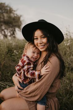 a woman holding a small child in her arms and smiling at the camera while wearing a cowboy hat