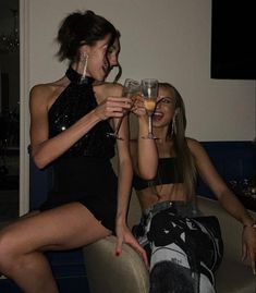 two women sitting on a couch holding wine glasses in their hands and laughing at each other