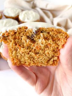 a hand holding a piece of carrot muffin with cream cheese frosting