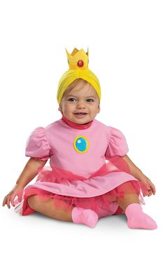 a baby wearing a pink princess costume sitting on the floor with her legs crossed and smiling at the camera