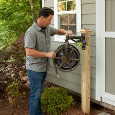 a man is working on an outdoor garden hose holder that has been attached to the side of a house