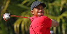 a man swinging a golf club on top of a lush green field with palm trees in the background