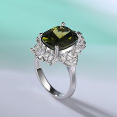 Celebrate one of the most unforgettable moments of your life with this joyous expression of love. This ring features a cushion cut center stone wrapped in a frame of marquise, emerald and trillion stones. All the stones sparkle perfectly from every angle, making the ring an eye-catcher everywhere.Carat Weight: 9.715 ctStone Size: 10*12 mmStone Type: Jeulia® StoneNumber of Stones: 1 Stone Shape: Elongated CushionStone Color: Peridot GreenCarat Weight: 2.225 ctStone Size: 3*3,1.5*3,2*4,1.2,2.5,2*1 Luxury Emerald Ring With Gemstone Accents For Wedding, Green Asscher Cut Ring With Diamond Accents, Luxury Green Cushion Cut Jewelry, Square Cut Emerald Ring With Accent Stones For Wedding, Green Cushion Cut Diamond Ring For Formal Occasions, Green Asscher Cut Cubic Zirconia Jewelry, Green Cubic Zirconia Asscher Cut Jewelry, Green Cushion Cut Emerald Ring With Accent Stones, Cushion Cut Rings For Wedding With May Birthstone