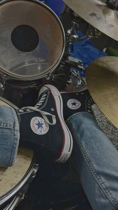 a pair of jeans and sneakers are sitting on top of a drum kit, with one person's feet resting on the drums