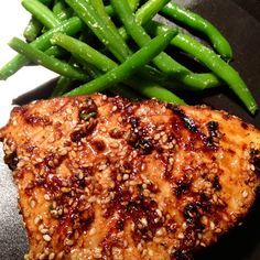 a piece of meat and some green beans on a black plate with a fork next to it