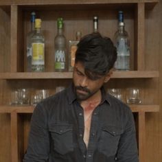 a man standing in front of a wooden shelf with bottles on it's shelves