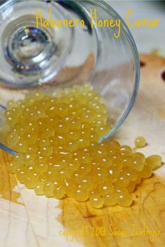 a glass filled with yellow beads sitting on top of a wooden table next to an orange leaf