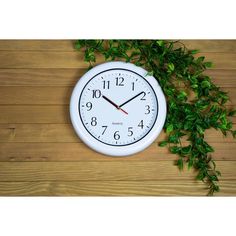 a white clock sitting on top of a wooden floor next to green plants and leaves