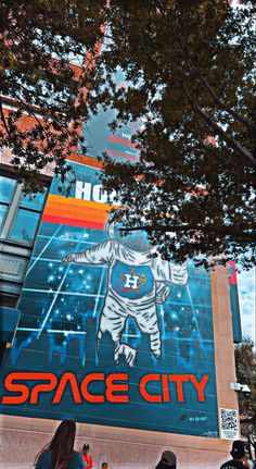 people are standing in front of a space city advertisement on the side of a building