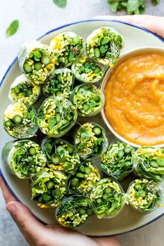 a person holding a plate with some artichokes and dipping sauce on it