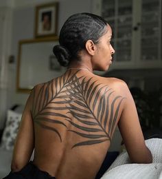 a woman sitting on top of a bed with a tattoo on the back of her body