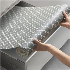 a person is holding a roll of fabric in front of a drawer that has drawers on it