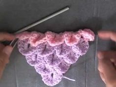 two hands holding a piece of crochet with yarn on it and knitting needles