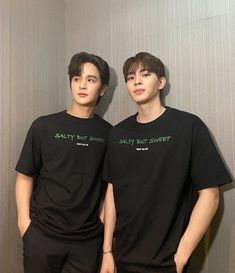 two young men standing next to each other wearing black shirts with green writing on them