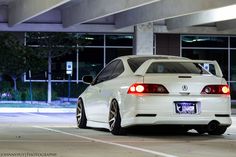 a white car parked in front of a building at night with its lights turned on