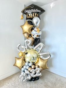 a graduation balloon tower in the corner of a room with congratulations balloons and decorations on it