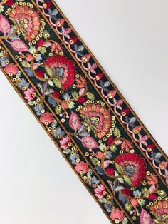 an embroidered ribbon with flowers and leaves on black fabric, hanging from a white wall