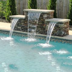 an outdoor pool with waterfall and stone wall