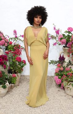 a woman standing in front of flowers wearing a long yellow dress with an open back