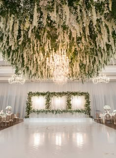 an elegant wedding setup with white flowers and greenery hanging from the ceiling, surrounded by chandeliers