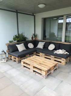 a couch made out of wooden pallets sitting on top of a cement floor next to a window