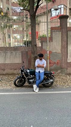 a man sitting on top of a motorcycle next to a tree