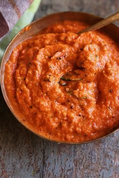 a wooden bowl filled with red sauce on top of a table next to a spoon