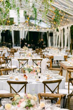 tables and chairs are set up in a tent for an outdoor wedding reception with white linens and greenery