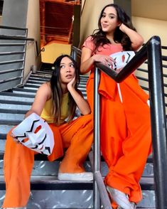 two women in orange outfits sitting on stairs