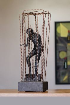 a sculpture is sitting on a table in front of a framed art piece with chains hanging from it's sides