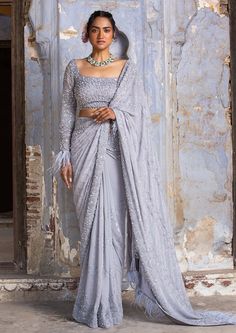 Editor's Note This set features a graceful grey georgette sari paired with a stunning organza full sleeves blouse. The blouse is adorned with self and silver beadwork, sequins, and crystals, adding a touch of glamour and elegance to the ensemble. The blouse also features feather fringes, creating a unique and eye-catching design. The grey ombre effect of the sari complements the silver embellishments on the blouse, resulting in a beautiful and cohesive look. Color: Gray Fabric: Sari: georgette, Saree With Full Sleeves, Sequinned Saree, Full Sleeves Blouse, Full Sleeves Blouse Designs, Crystal Work, Silver Blouse, Pure Georgette Sarees, Sequin Saree, Grey Saree