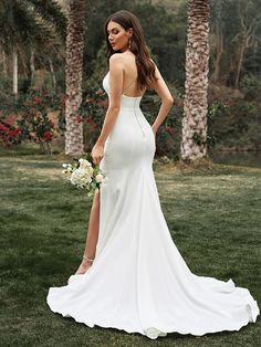 a woman in a white wedding dress standing on the grass with palm trees behind her