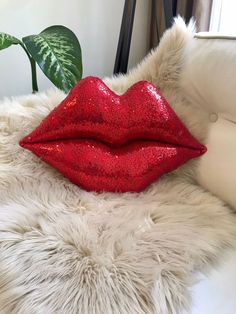 a red glittered lip sitting on top of a white fur covered bed next to a plant