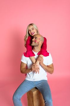 a man holding a woman in his arms on top of a wooden block against a pink background