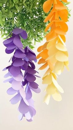 three different colors of paper flowers hanging from a tree branch with green leaves in the background