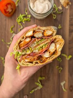 a person holding up a sandwich with meat and lettuce on it next to a jar of mayonnaise