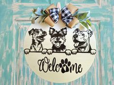 a door hanger with three dogs on it and the word welcome is painted in black