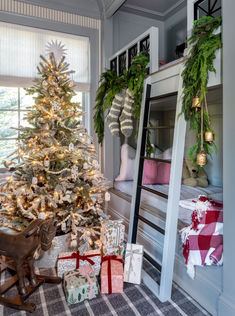 a christmas tree with presents under it in front of a bunk bed and window sill