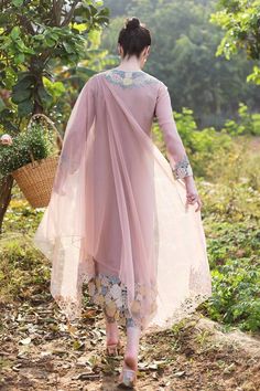 a woman in a pink dress walking down a dirt road