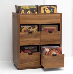 a wooden shelf with several drawers and cd's in it on top of a white floor