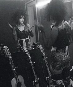 a woman standing in front of a mirror next to guitars