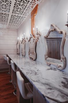 a long counter with several mirrors on it and white chairs in front of the counter