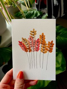 a hand holding up a card with watercolor leaves on it