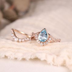 two wedding rings with an aqua blue topazte surrounded by white pearls and diamonds