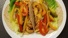 two tacos with chicken, peppers and lettuce on a white plate