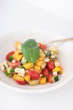 a white plate topped with a salad next to a silver spoon on top of a table