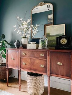 a wooden dresser sitting next to a mirror and vase on top of a hard wood floor